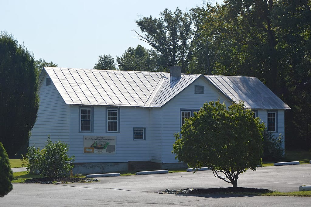 white one-story building with parking lot in the foreground and trees in the background