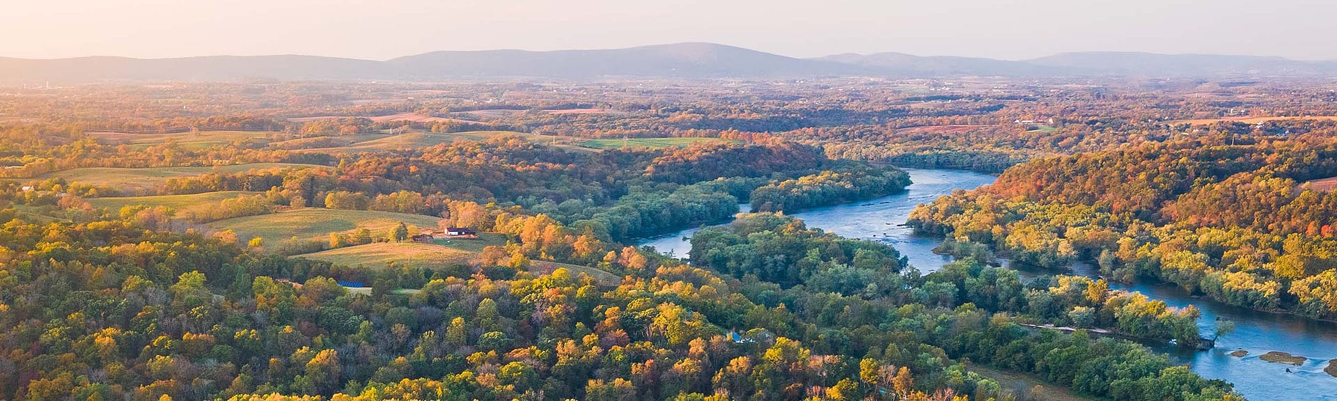 drone image of the Potomac River flowing through a forested rural landscape, with mountains on the horizon